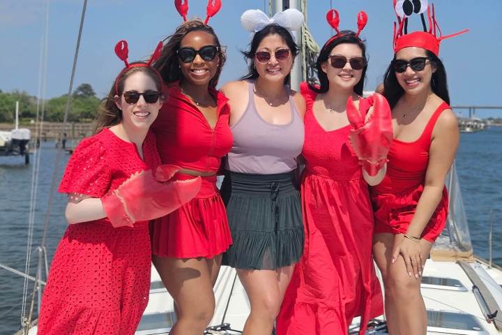 Five people on a boat, dressed in red, some with lobster hats, smiling.