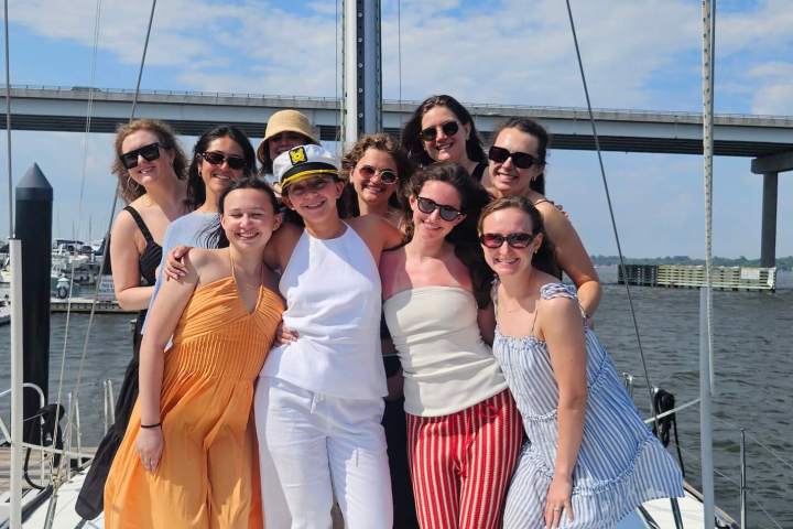 Group of nine women posing on a boat under a partly cloudy sky.