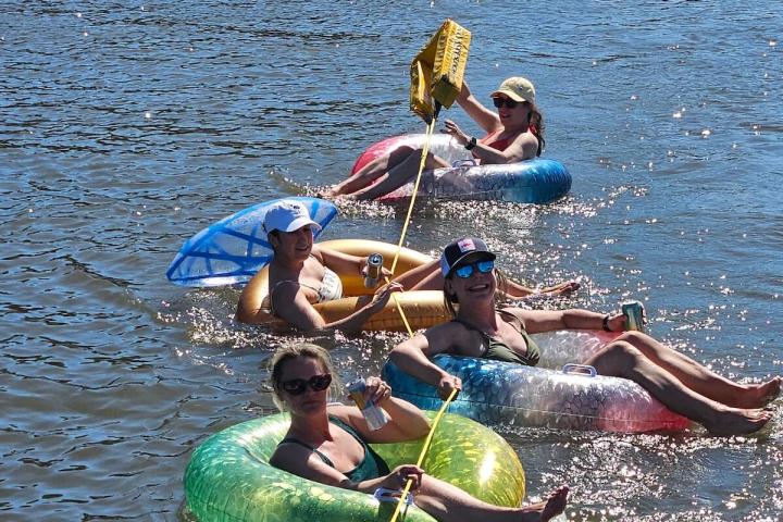 Four people floating on tubes in a river, connected by a rope.