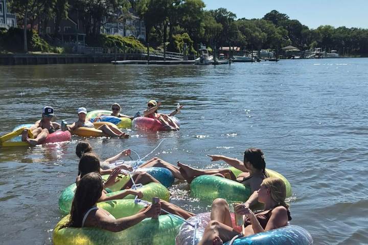 People relaxing in colorful inflatable tubes on a river, holding drinks under a clear blue sky.