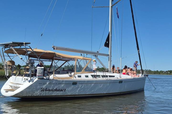 Sailboat named Windchaser with people on deck, calm water, clear sky.