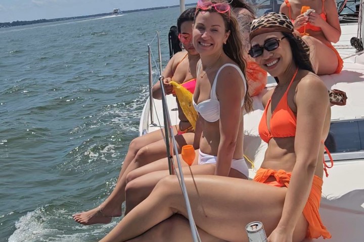 Group of people in swimwear sitting on a sailboat in the ocean.