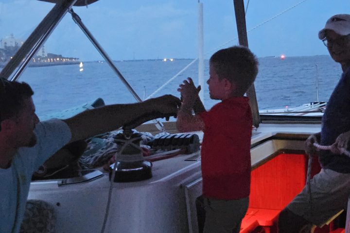Child on a boat with two adults, evening sky and water in background.