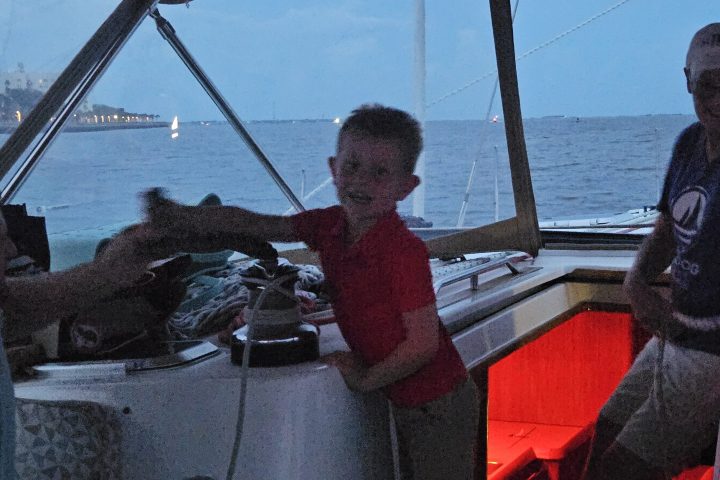 Two people and a child on a boat in the evening; interior is lit with red light.