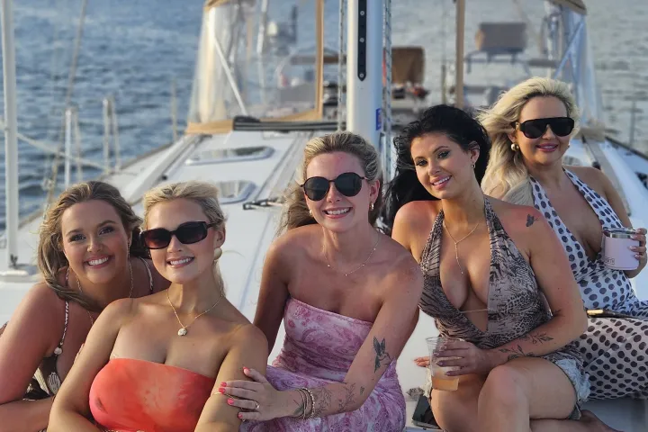 Five women in sunglasses posing on a sailboat on a sunny day.