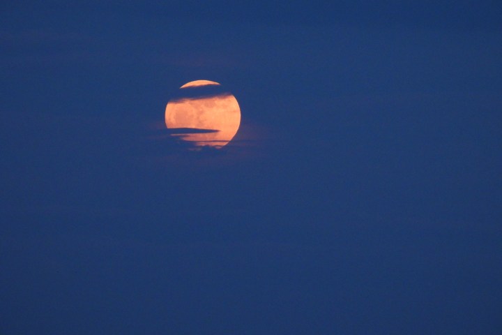 Orange full moon partially obscured by clouds in a dark blue night sky.