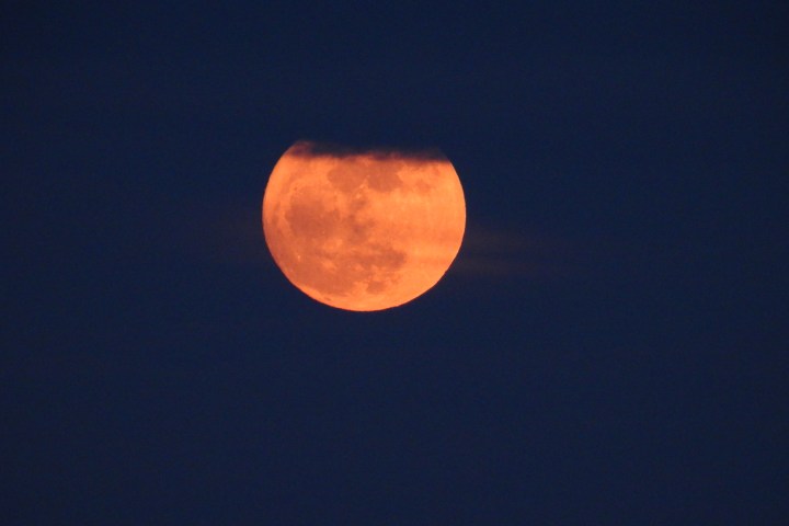 Partially cloud-covered orange moon in a dark sky.