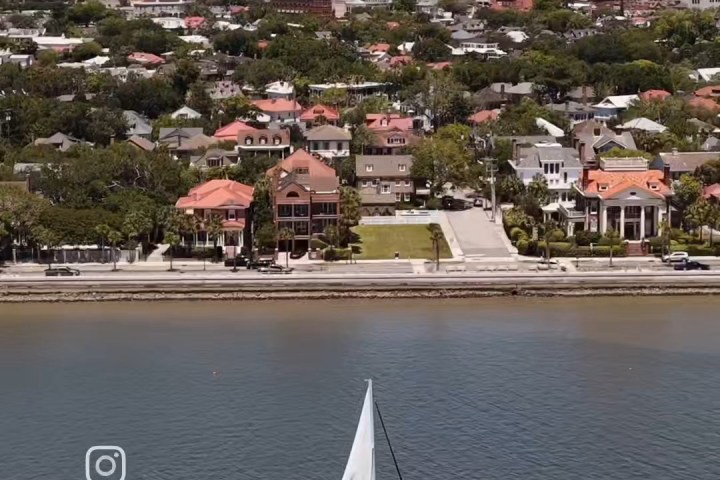 Sailboat on a river with a city and bridge in the background.