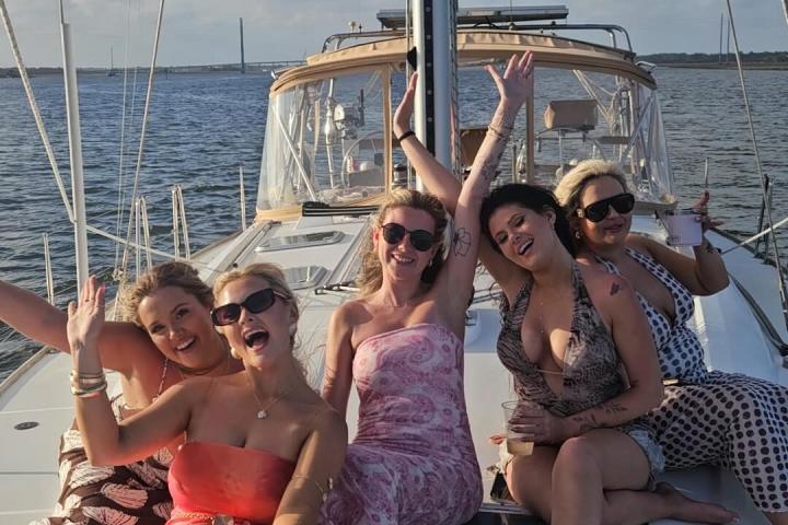 Group of five women smiling and sitting on a sailboat deck.