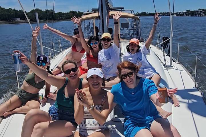 Group of people smiling and posing on a sailboat on a sunny day.