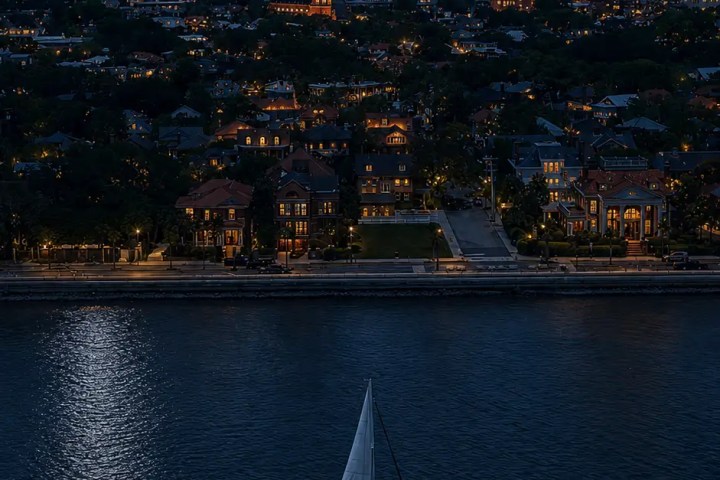 Sailboat on river at night, city lights and bridge under full moon.