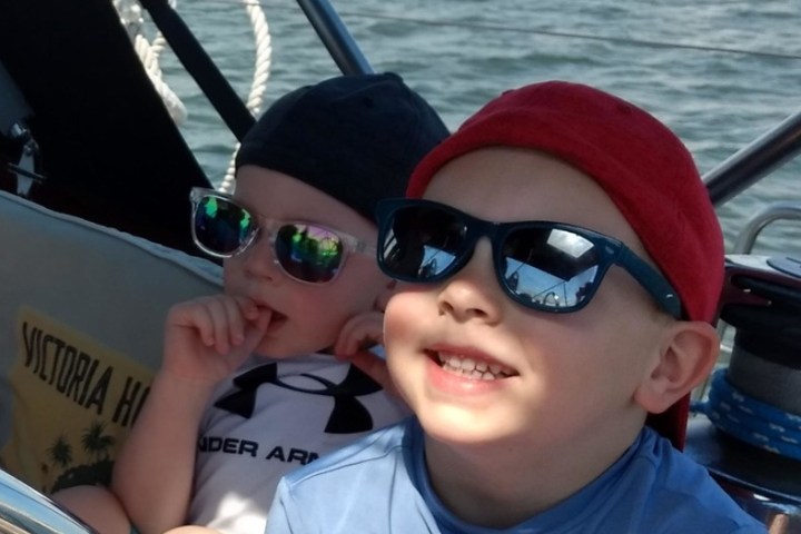 a little boy wearing a hat and sunglasses sitting on a boat
