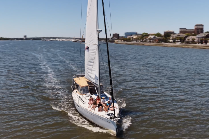 Sailboat on a river with city buildings in the background.