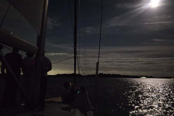 Nighttime boat scene with moonlight reflecting on water.
