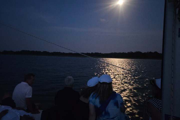 People on a boat at night, looking at a bright full moon over water.