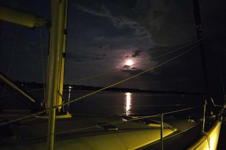Moonlit sailboat on calm water at night with cloudy sky.