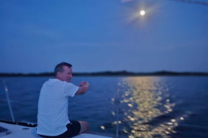 Person on a boat at night, looking at the moon reflecting on water.