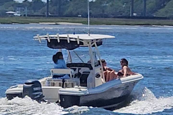 Small motorboat with people on a river, bridge in background.