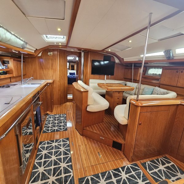 Interior of a wooden yacht with kitchen, seating, and TV, featuring patterned rugs.
