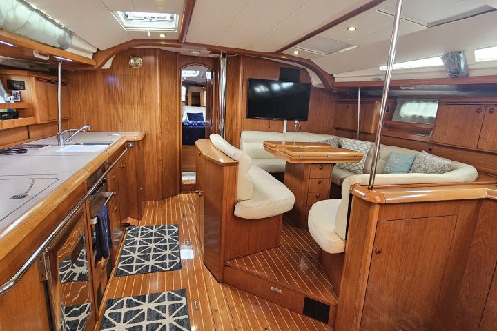 Interior of a wooden yacht with kitchen, seating, and TV, featuring patterned rugs.