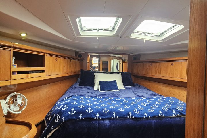Cozy yacht cabin with a bed, blue anchor-patterned blanket, and wooden interior.