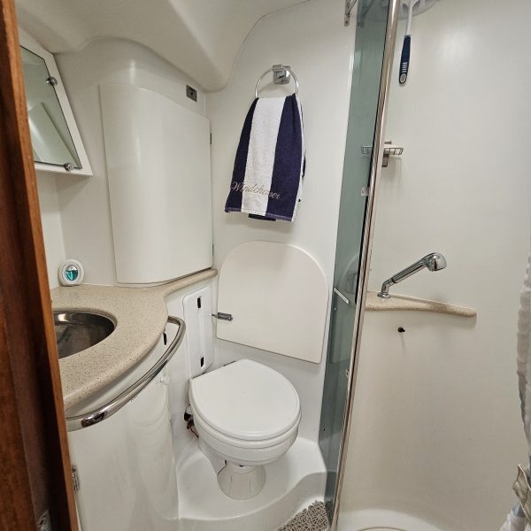Compact boat bathroom with a toilet, sink, towel, and a small shower area.