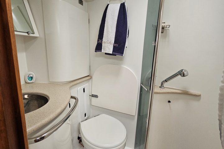 Compact boat bathroom with a toilet, sink, towel, and a small shower area.