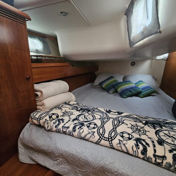 Cozy boat cabin with a double bed, striped pillows, and maritime-themed blanket.