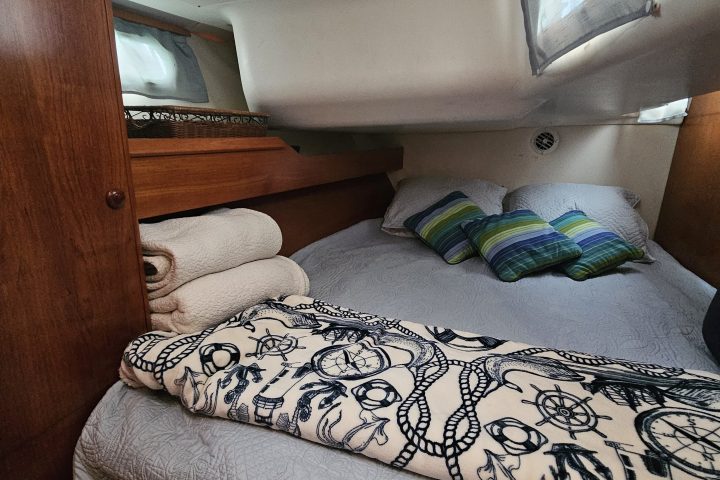 Cozy boat cabin with a double bed, striped pillows, and maritime-themed blanket.