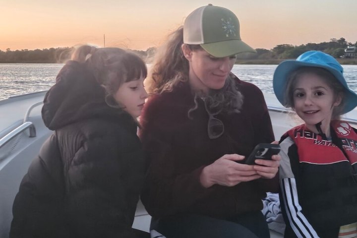 Woman and two children seated on a boat at sunset.