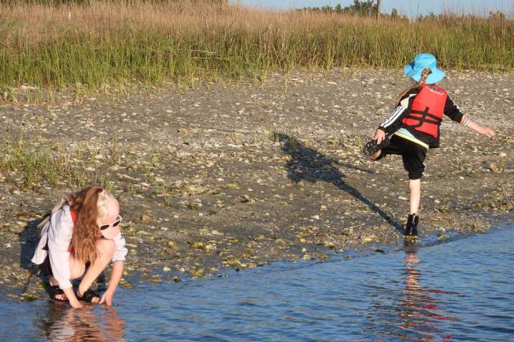 Two children playing by the water; one touches water, the other stands on one foot.