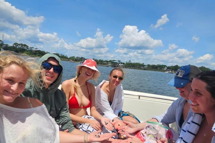Group of people smiling and sitting on a boat under a sunny sky.