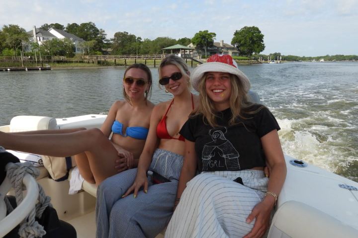 Three smiling women on a boat with a scenic river background.