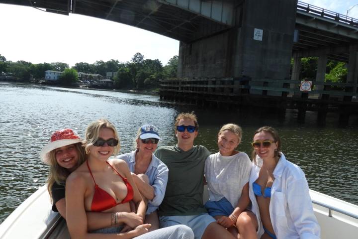 Group of six people smiling on a boat under a bridge.