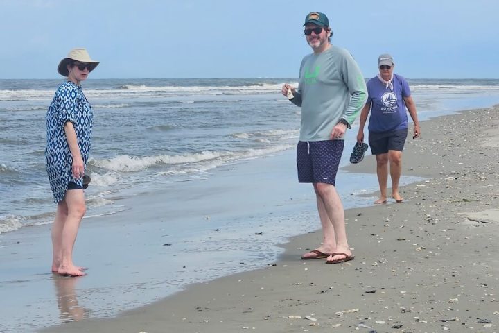 Three people walking on a sandy beach near the shoreline.