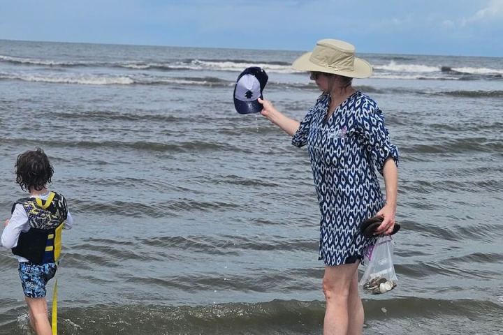 Woman and child walking in ocean waves, woman holds hat and seashells.