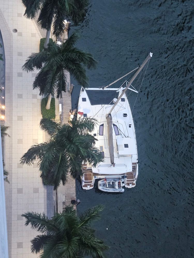 Aerial view of a docked sailboat with palm trees and a walkway beside it.