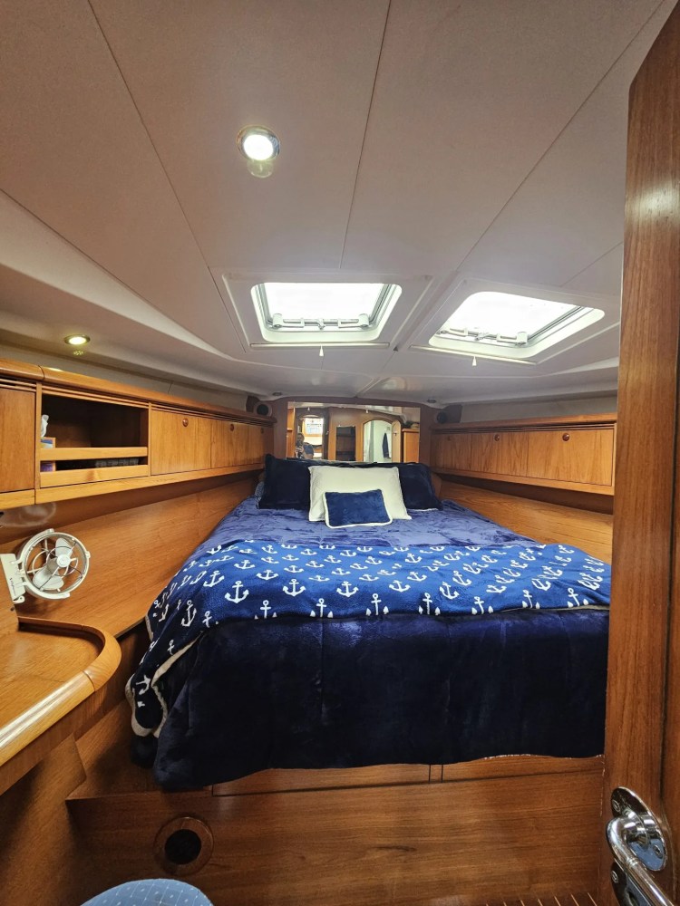 Cozy yacht cabin with a bed, blue anchor-patterned blanket, and overhead skylights.