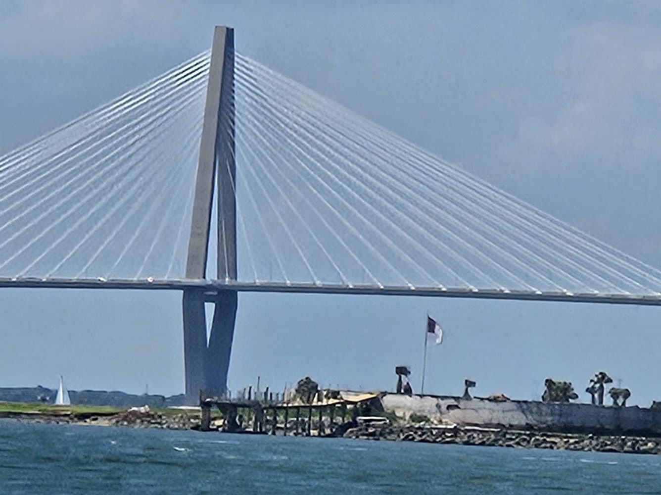 Side view of a cable-stayed bridge over water with cloudy sky.