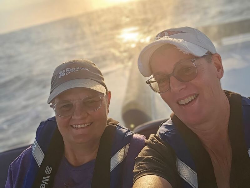Two people on a boat wearing life jackets with the sun setting over the ocean.
