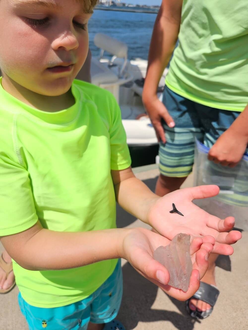 Child holding a large fossilized tooth by the water.
