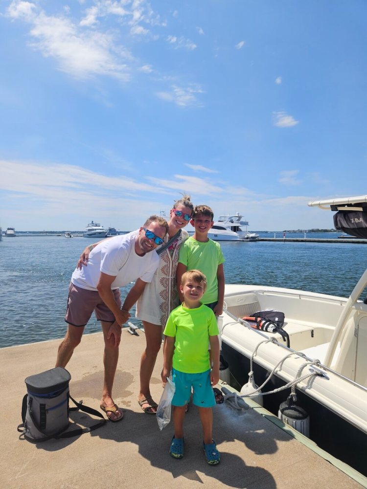 Family of four smiling on a dock beside a boat on a sunny day.
