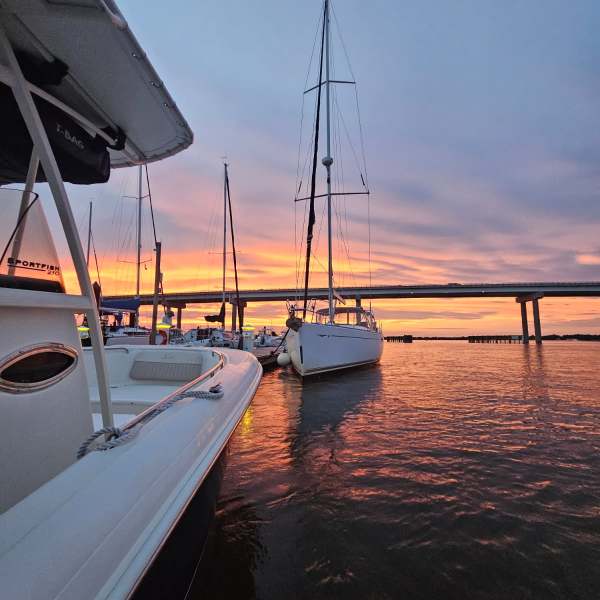 Sailboats on calm water at sunset with a bridge in the background.