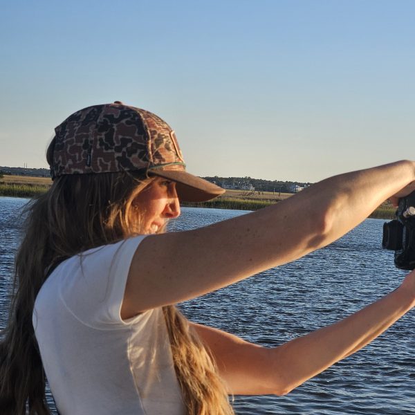 Person in a cap takes photos by the water's edge.