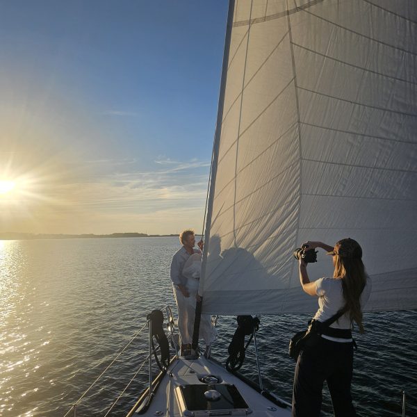 People sailing at sunset, one taking photos on a boat's deck.