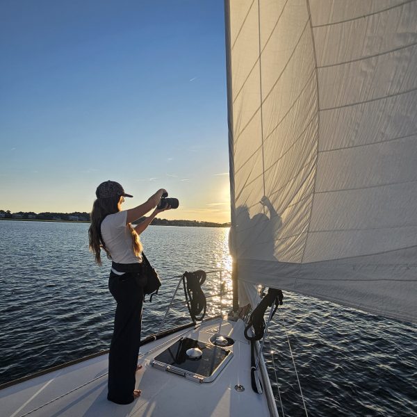 Person photographing sunset on a sailboat, with the sails in view.