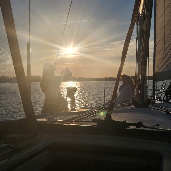 Silhouette of a person on a sailboat at sunset.