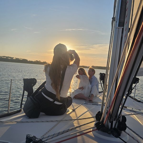 People sitting on a sailboat at sunset, facing each other.