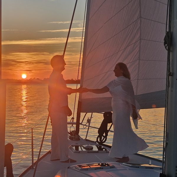 Two people on a sailboat at sunset, holding the sail ropes.