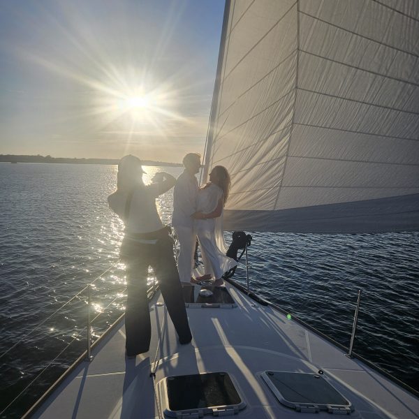 People on a sailboat during sunset with sails up on the water.